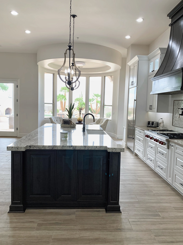 Design ideas for a large transitional l-shaped open plan kitchen in Phoenix with a farmhouse sink, raised-panel cabinets, white cabinets, quartz benchtops, white splashback, ceramic splashback, stainless steel appliances, cement tiles, with island, grey floor and beige benchtop.