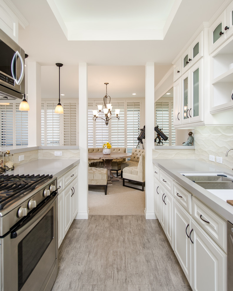 Photo of a small traditional galley separate kitchen in Los Angeles with an undermount sink, glass-front cabinets, white cabinets, quartz benchtops, beige splashback, ceramic splashback, stainless steel appliances and porcelain floors.