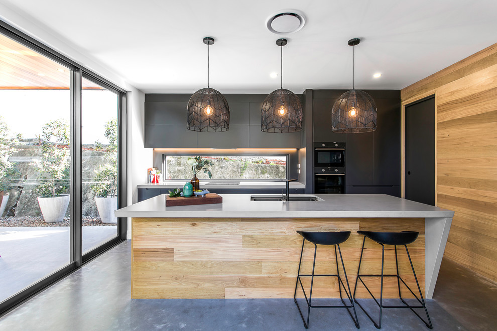 Photo of a mid-sized contemporary galley eat-in kitchen in Brisbane with a drop-in sink, flat-panel cabinets, black cabinets, mirror splashback, black appliances, concrete floors, multiple islands and grey floor.
