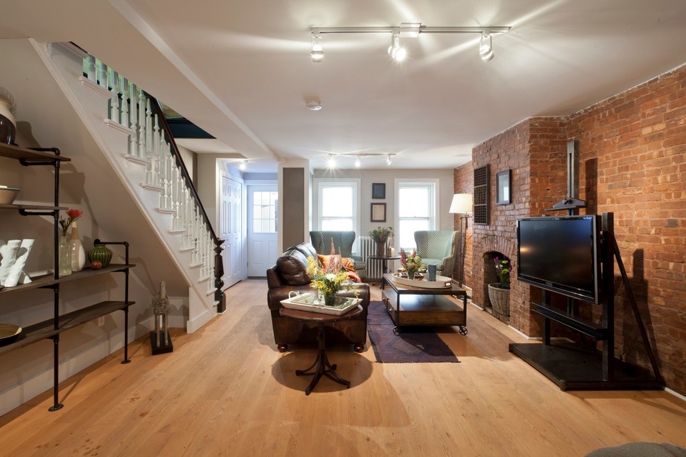 This is an example of a traditional living room in New York with grey walls, light hardwood floors, a standard fireplace and a brick fireplace surround.