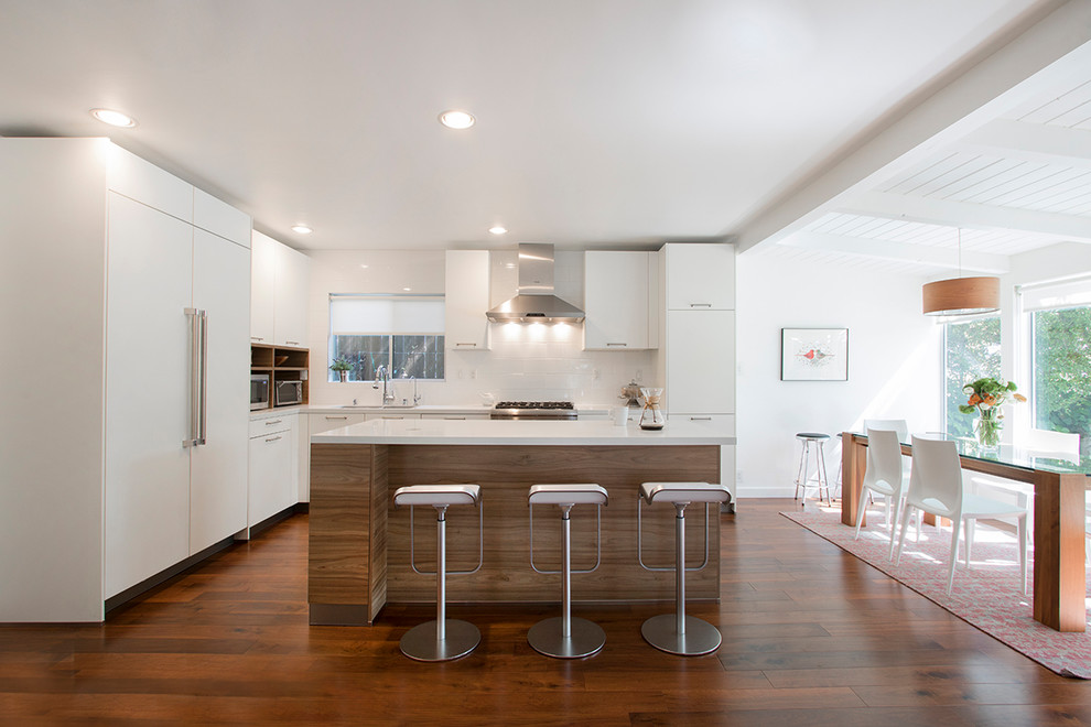 This is an example of a mid-sized contemporary l-shaped eat-in kitchen in Los Angeles with a drop-in sink, flat-panel cabinets, medium wood cabinets, quartzite benchtops, white splashback, porcelain splashback, stainless steel appliances, laminate floors, with island, brown floor and white benchtop.