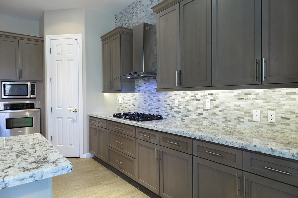 Mid-sized transitional u-shaped laminate floor and beige floor eat-in kitchen photo in Phoenix with a drop-in sink, shaker cabinets, medium tone wood cabinets, granite countertops, beige backsplash, glass sheet backsplash, stainless steel appliances, a peninsula and beige countertops