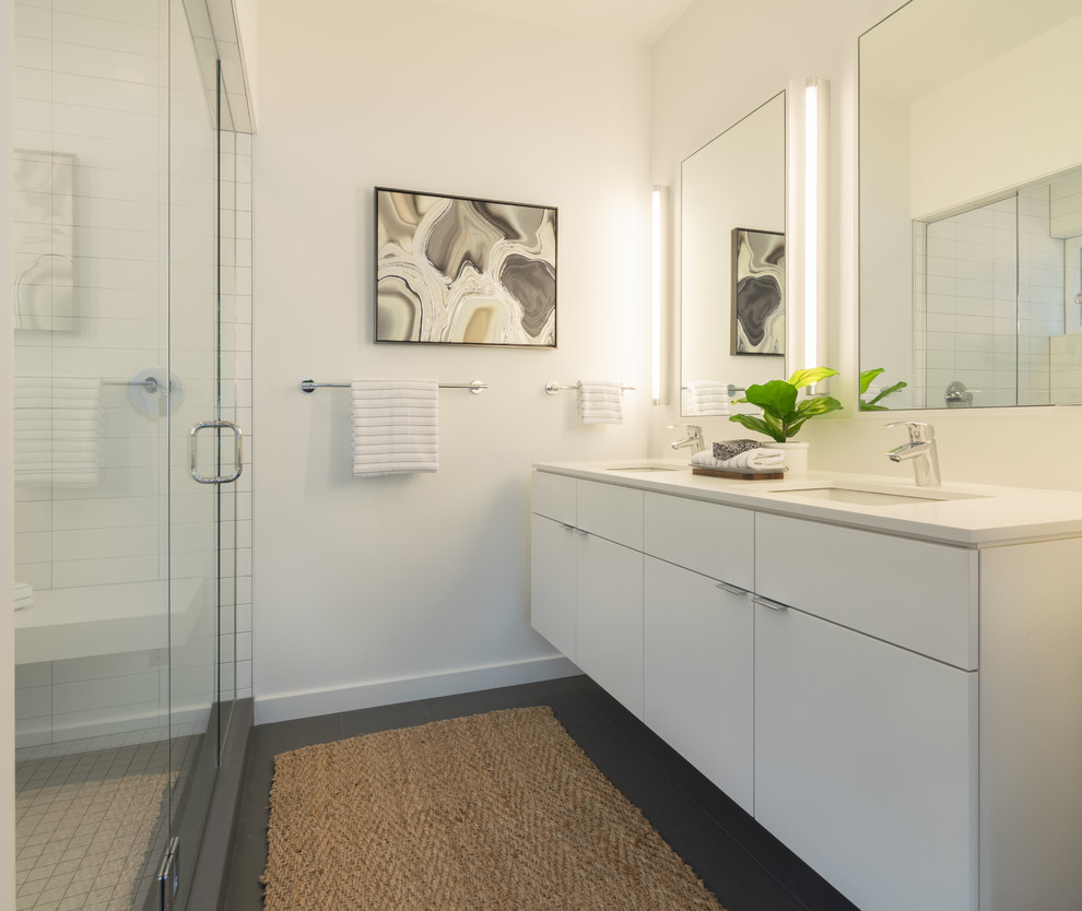 Photo of a mid-sized modern master bathroom in Seattle with flat-panel cabinets, white cabinets, an alcove shower, a one-piece toilet, white tile, ceramic tile, white walls, cement tiles, an undermount sink, solid surface benchtops, grey floor, a hinged shower door and white benchtops.