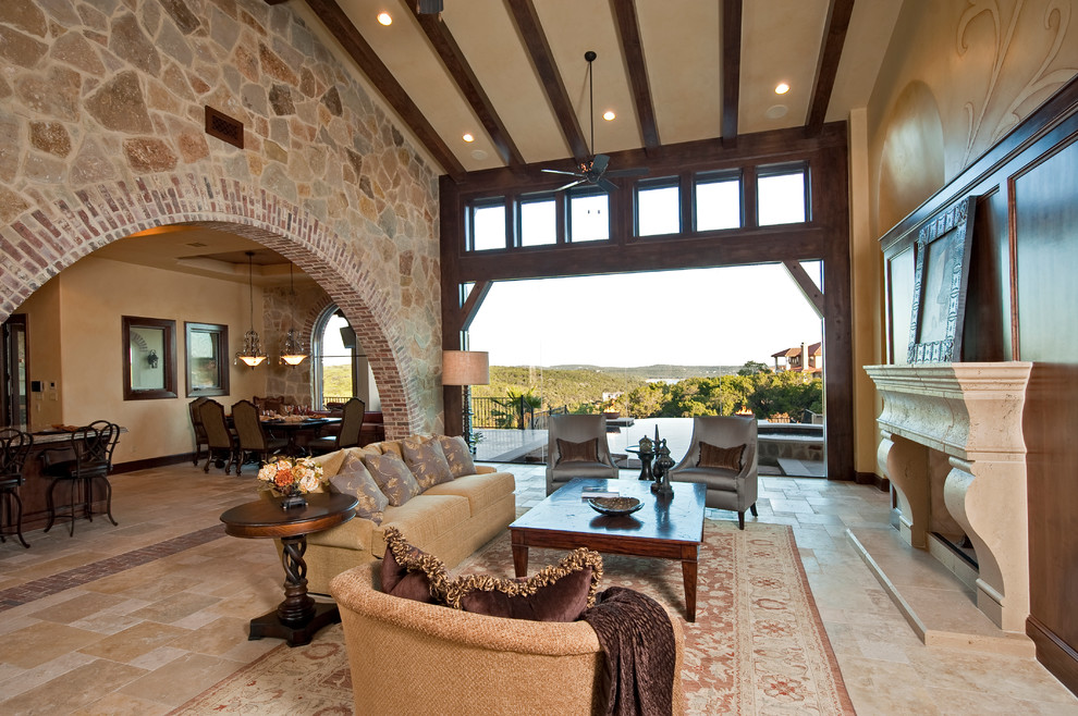 This is an example of an expansive mediterranean formal open concept living room in Austin with beige walls, travertine floors, a standard fireplace, a stone fireplace surround, a concealed tv and beige floor.