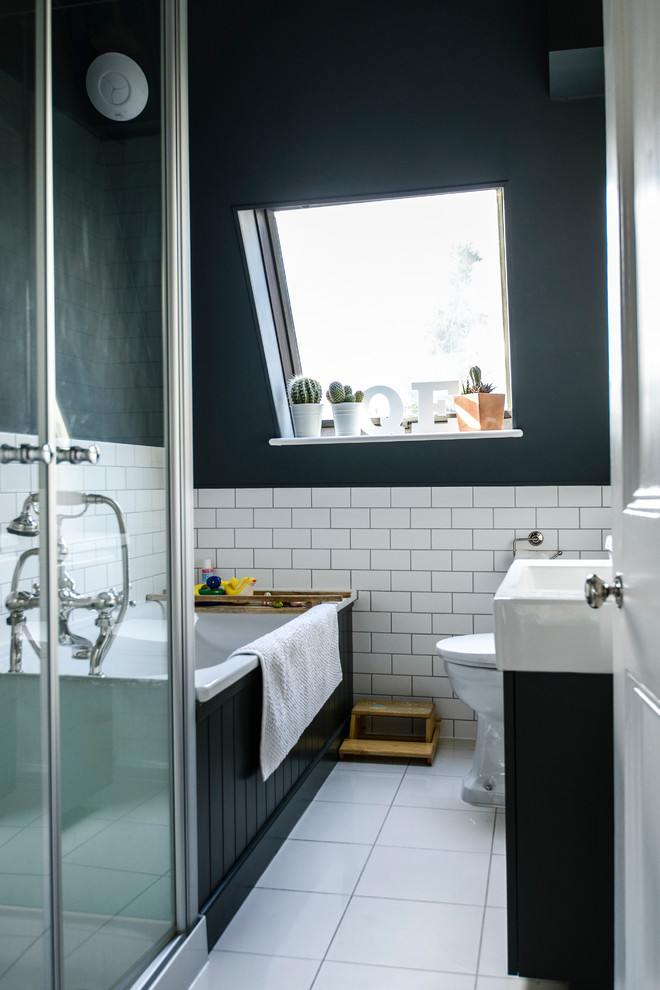 Photo of a transitional bathroom in London with an integrated sink, black cabinets, a drop-in tub and black walls.