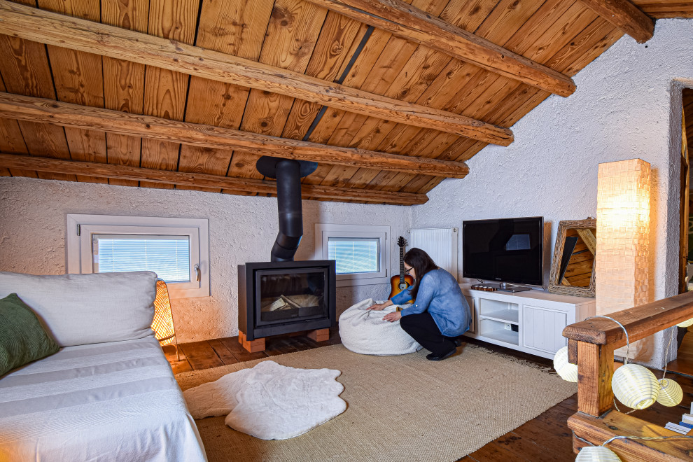 На фото: открытая гостиная комната среднего размера в стиле рустика с белыми стенами, деревянным полом, оранжевым полом, балками на потолке и печью-буржуйкой с