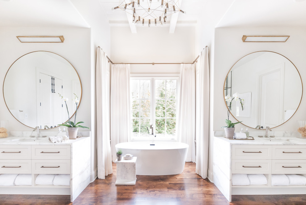 Design ideas for a transitional master bathroom in Nashville with shaker cabinets, white cabinets, a freestanding tub, white walls, dark hardwood floors, an undermount sink, brown floor and white benchtops.