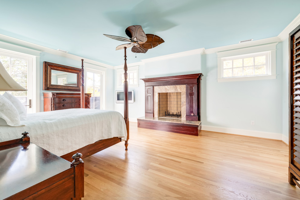 Large traditional master bedroom in Other with blue walls, light hardwood floors, a standard fireplace, a wood fireplace surround and brown floor.