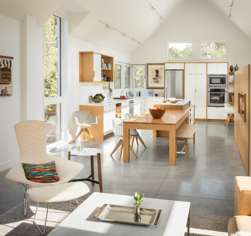 Bright open-plan kitchen with light plywood cabinets, large windows and modern white finishes