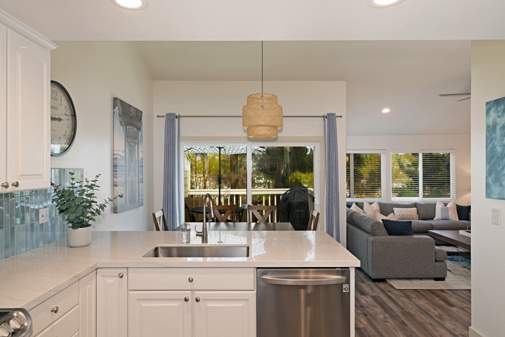 Design ideas for a mid-sized beach style l-shaped open plan kitchen in San Diego with an undermount sink, raised-panel cabinets, white cabinets, blue splashback, ceramic splashback, stainless steel appliances, vinyl floors, a peninsula, grey floor, white benchtop, vaulted and quartzite benchtops.