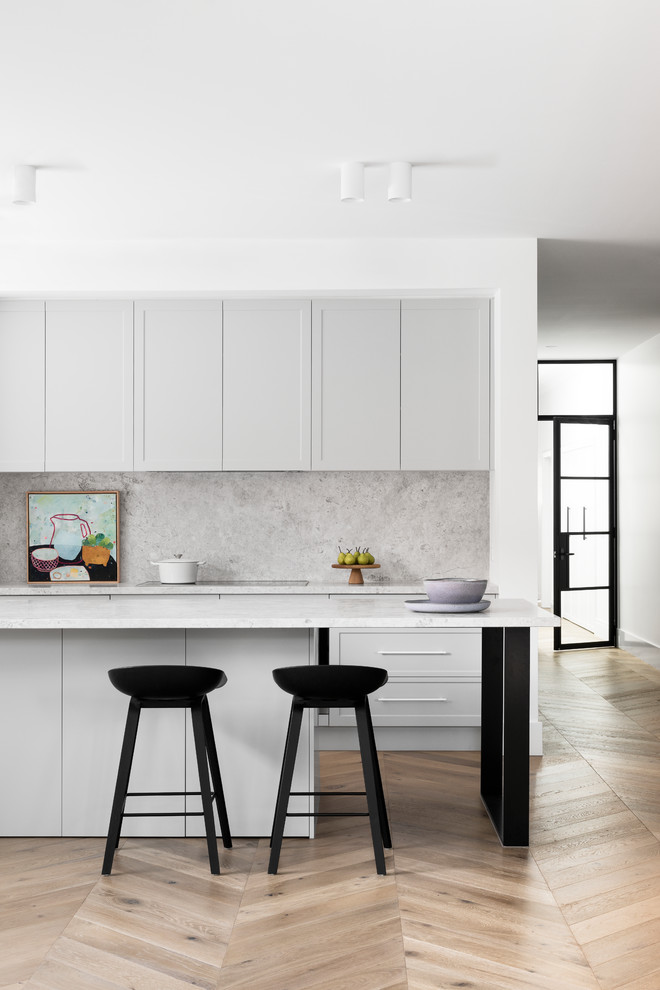 Design ideas for a large contemporary galley open plan kitchen in Melbourne with shaker cabinets, grey cabinets, marble benchtops, grey splashback, marble splashback, black appliances, medium hardwood floors, multiple islands, brown floor and grey benchtop.