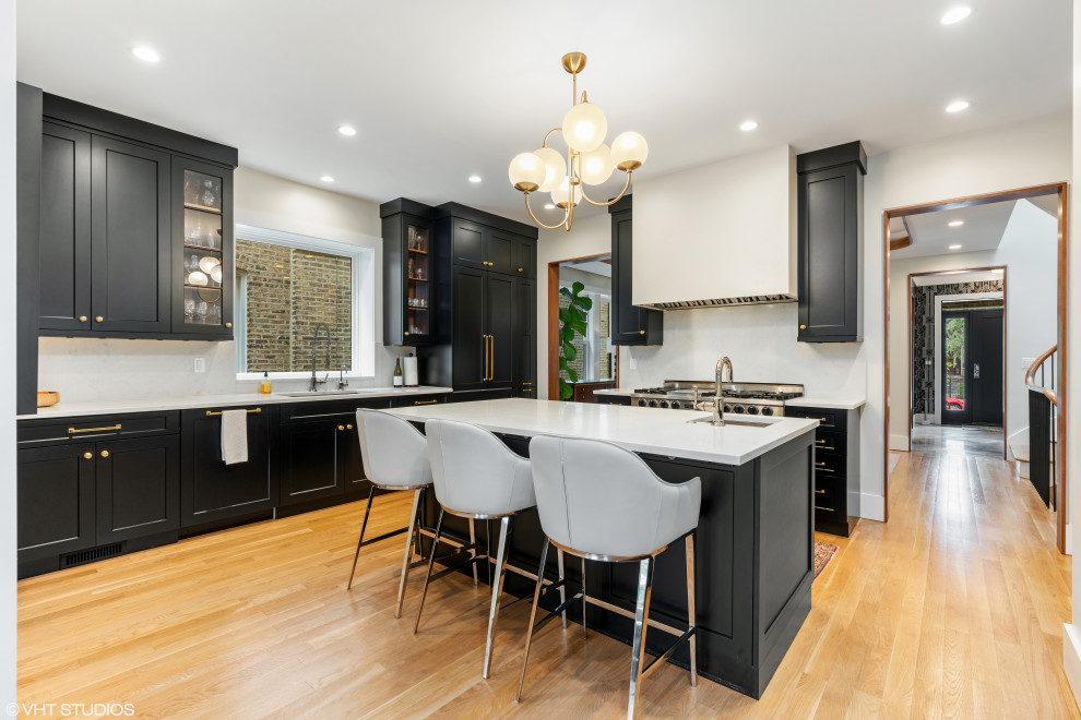 Example of a transitional light wood floor kitchen design in Chicago with a single-bowl sink, shaker cabinets, black cabinets, stainless steel appliances and an island