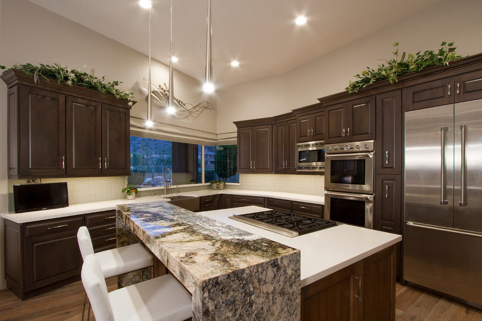 Eat-in kitchen - mid-sized transitional l-shaped light wood floor and brown floor eat-in kitchen idea in Phoenix with a farmhouse sink, shaker cabinets, quartzite countertops, glass sheet backsplash, stainless steel appliances, an island, dark wood cabinets, beige backsplash and white countertops