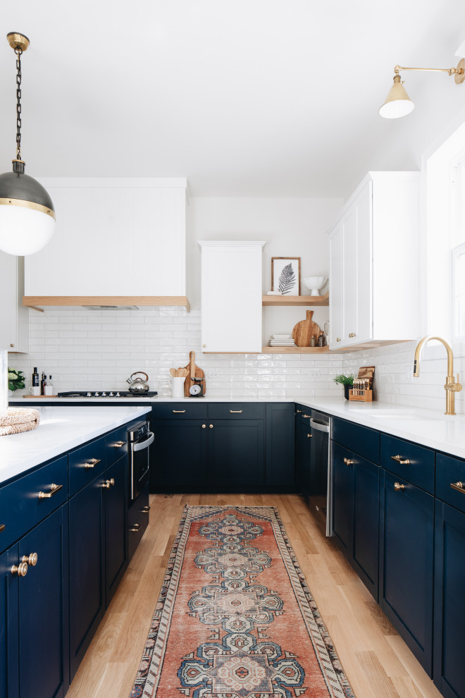 This is an example of a transitional l-shaped kitchen in Chicago with an undermount sink, shaker cabinets, blue cabinets, white splashback, subway tile splashback, light hardwood floors, with island, beige floor and white benchtop.