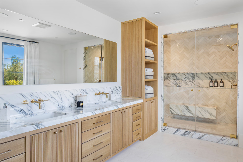 Photo of a large mediterranean bathroom in Los Angeles with beaded inset cabinets, light wood cabinets, a freestanding tub, a double shower, a one-piece toilet, multi-coloured tile, marble, white walls, limestone floors, with a sauna, an undermount sink, marble benchtops, white floor, a hinged shower door, multi-coloured benchtops, a shower seat, a double vanity and a built-in vanity.