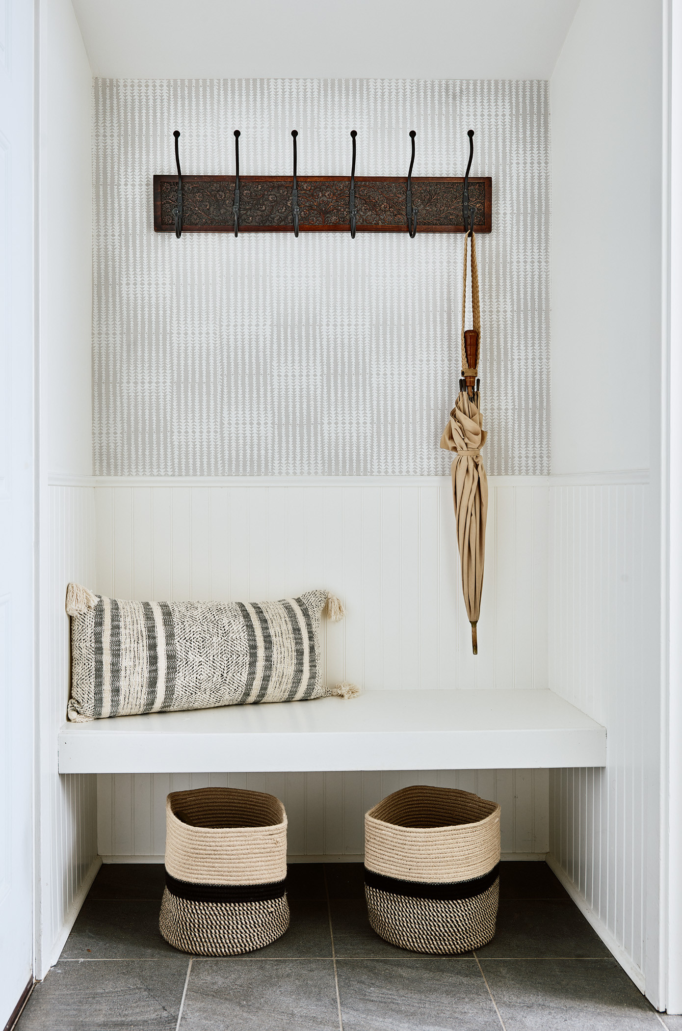 Neutral Mudroom With Grasscloth Wallpaper Features a Built-In Storage Bench  Topped With Multicolor Throw Pillows