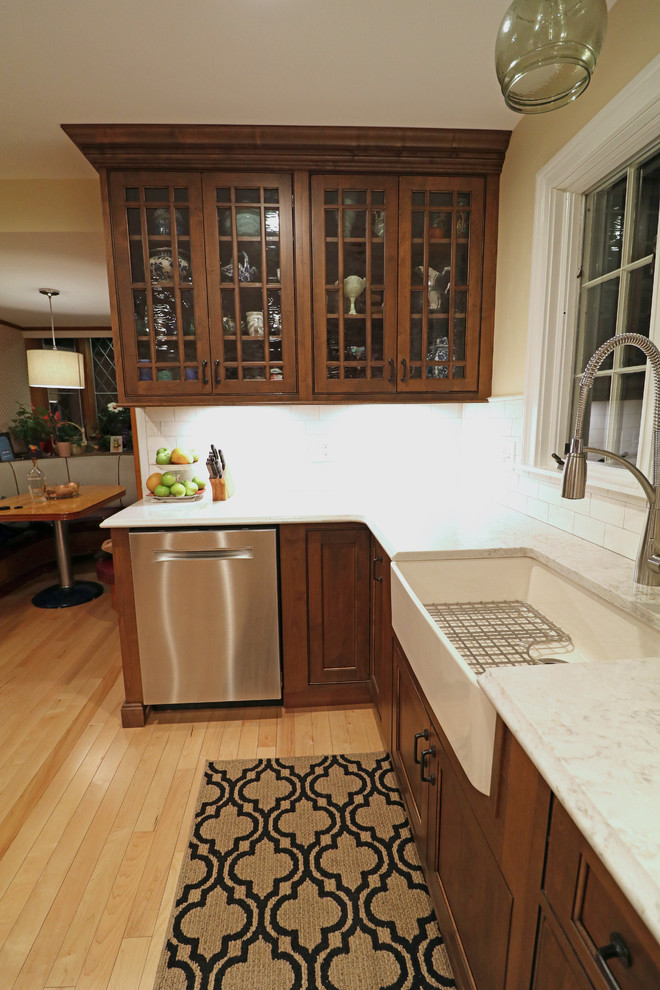 This is an example of a mid-sized arts and crafts l-shaped kitchen pantry in Boston with a farmhouse sink, beaded inset cabinets, dark wood cabinets, quartz benchtops, beige splashback, travertine splashback, stainless steel appliances, light hardwood floors, no island and beige floor.