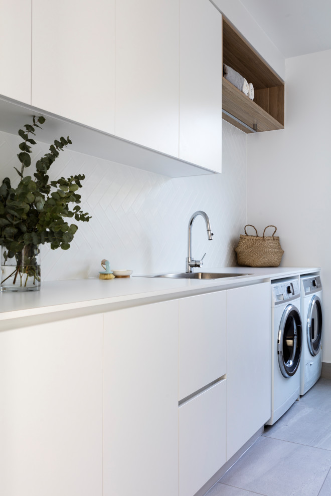 Beach style galley laundry room in Sunshine Coast with flat-panel cabinets, white cabinets, a side-by-side washer and dryer, grey floor and white benchtop.