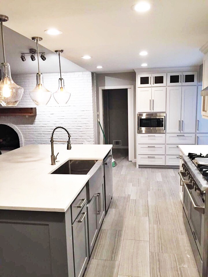Photo of a mid-sized modern galley eat-in kitchen in Dallas with a farmhouse sink, raised-panel cabinets, grey cabinets, quartz benchtops, white splashback, ceramic splashback, stainless steel appliances, porcelain floors, with island and grey floor.