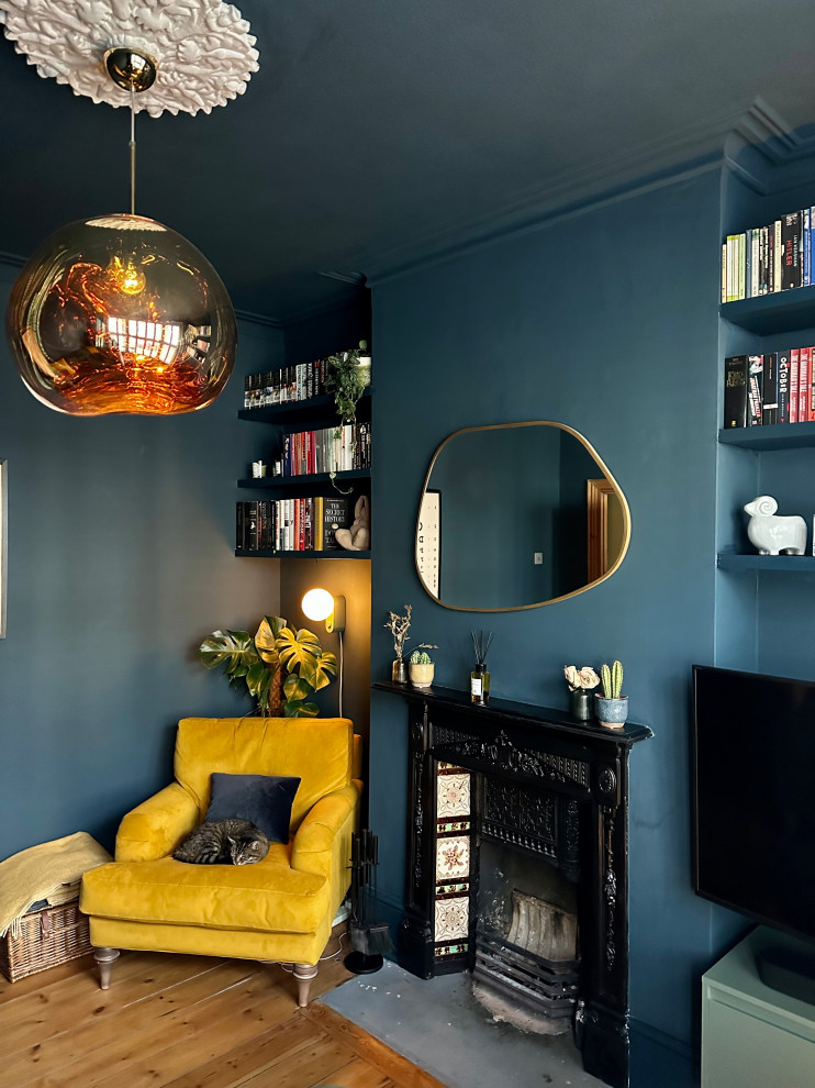 Cette photo montre un salon tendance de taille moyenne et fermé avec un mur bleu, un sol en bois brun, une cheminée standard, un manteau de cheminée en métal, un téléviseur fixé au mur et un sol marron.