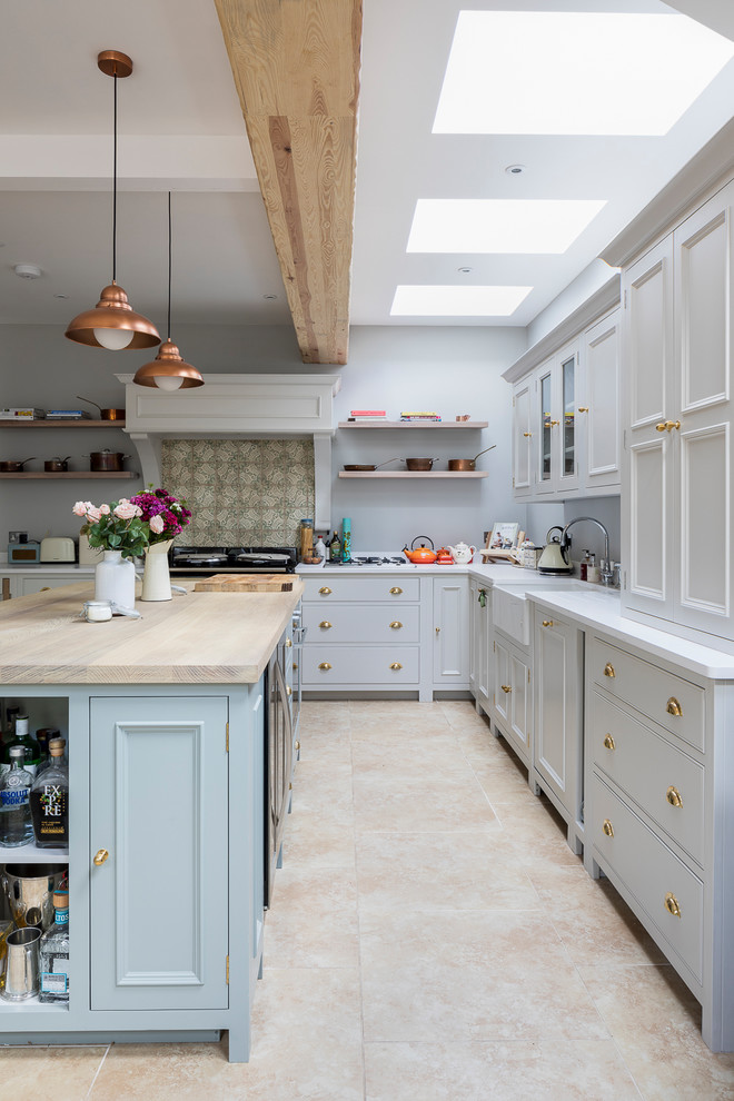 Mid-sized country l-shaped eat-in kitchen in London with a farmhouse sink, shaker cabinets, grey cabinets, solid surface benchtops, green splashback, porcelain splashback, stainless steel appliances, limestone floors, with island and beige floor.