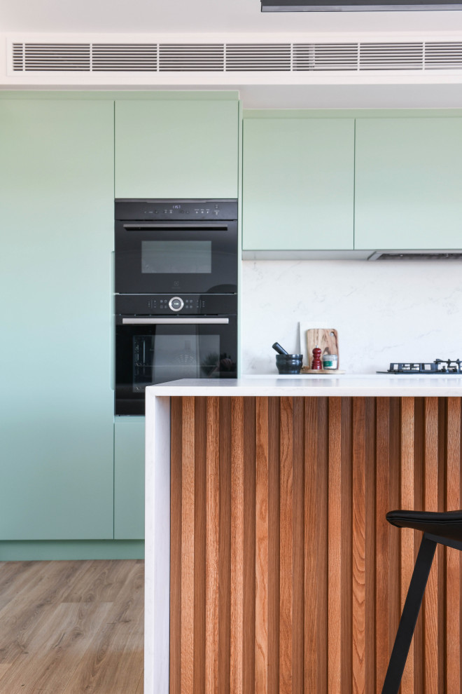 This is an example of a mid-sized scandinavian u-shaped open plan kitchen in Sydney with an undermount sink, green cabinets, quartz benchtops, white splashback, ceramic splashback, black appliances, with island, brown floor and white benchtop.