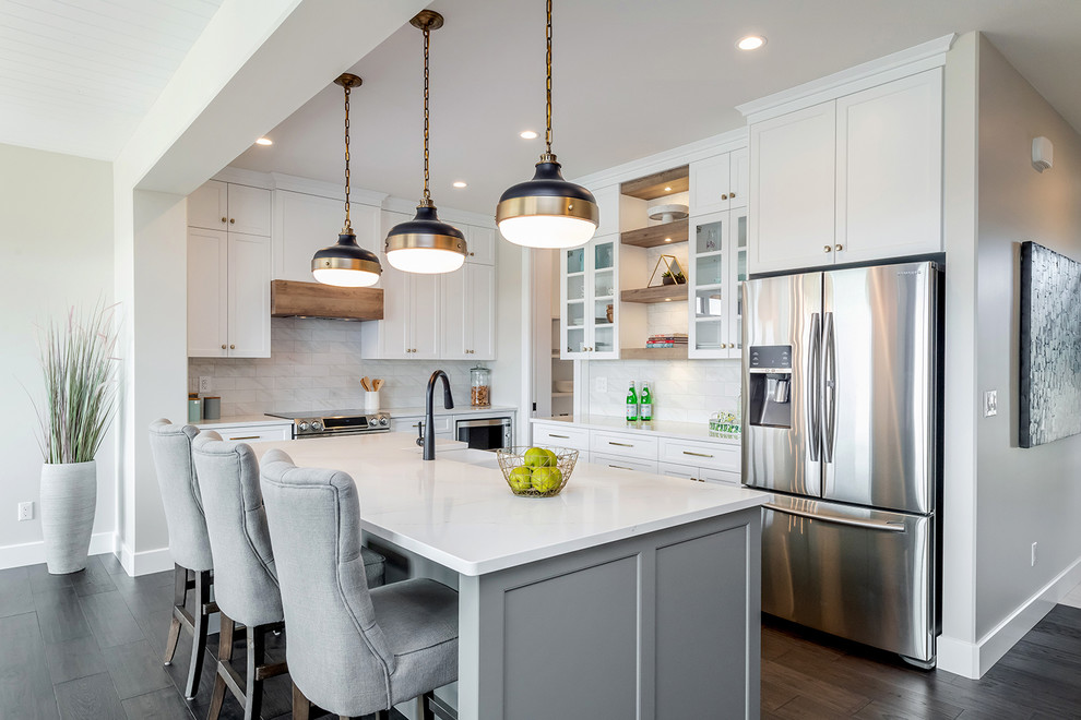 Transitional l-shaped dark wood floor and brown floor kitchen photo with a farmhouse sink, shaker cabinets, white cabinets, stainless steel appliances, an island and white countertops