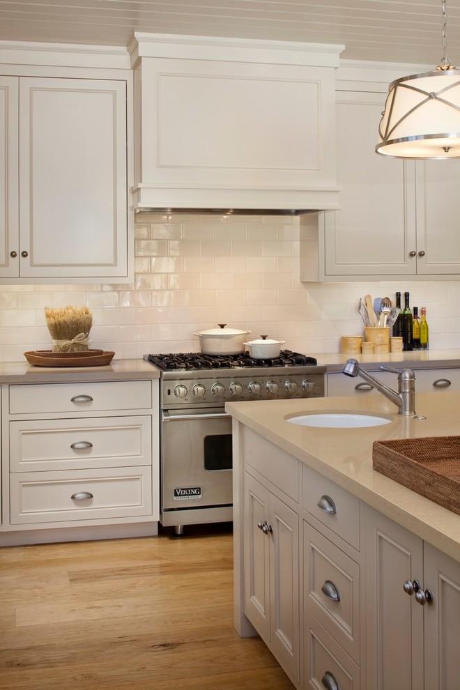 Design ideas for a mid-sized country u-shaped eat-in kitchen in San Francisco with a farmhouse sink, raised-panel cabinets, white cabinets, soapstone benchtops, white splashback, stone tile splashback, stainless steel appliances, light hardwood floors, with island and brown floor.