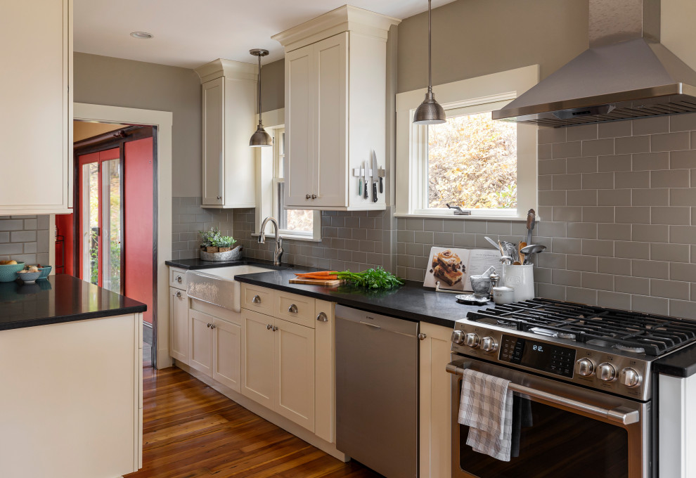 Kitchen - mid-sized transitional galley light wood floor kitchen idea in Boston with a farmhouse sink, shaker cabinets, white cabinets, granite countertops, gray backsplash, subway tile backsplash, stainless steel appliances, no island and black countertops