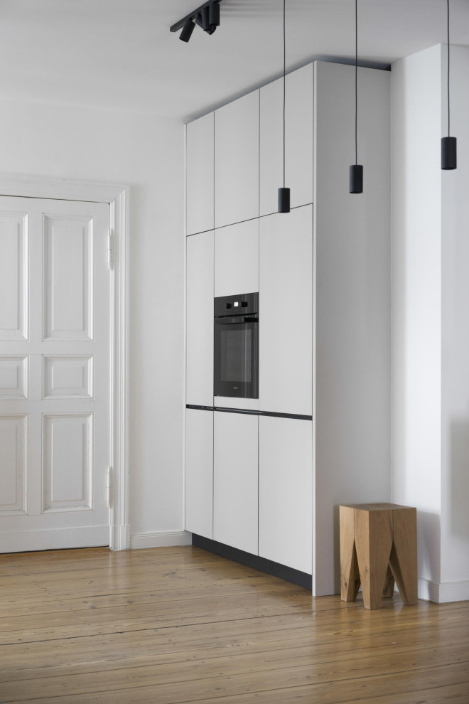 This is an example of a large modern single-wall eat-in kitchen in Berlin with a drop-in sink, flat-panel cabinets, beige cabinets, concrete benchtops, white splashback, mosaic tile splashback, panelled appliances, light hardwood floors, no island and grey benchtop.
