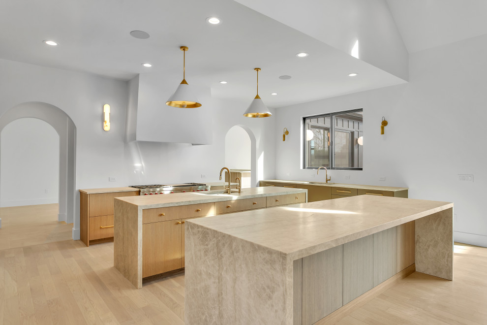 Open concept kitchen - large transitional u-shaped light wood floor, beige floor and vaulted ceiling open concept kitchen idea with an undermount sink, flat-panel cabinets, light wood cabinets, quartzite countertops, white backsplash, paneled appliances, two islands and beige countertops