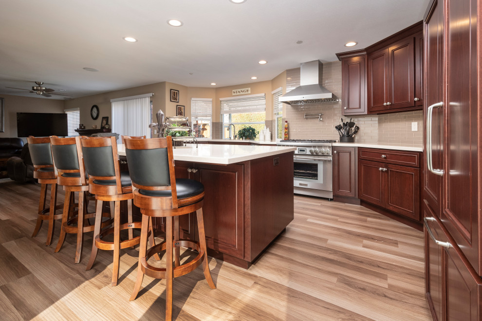 Large transitional l-shaped open plan kitchen in San Francisco with an undermount sink, shaker cabinets, medium wood cabinets, quartzite benchtops, beige splashback, subway tile splashback, stainless steel appliances, porcelain floors, with island, beige floor and white benchtop.