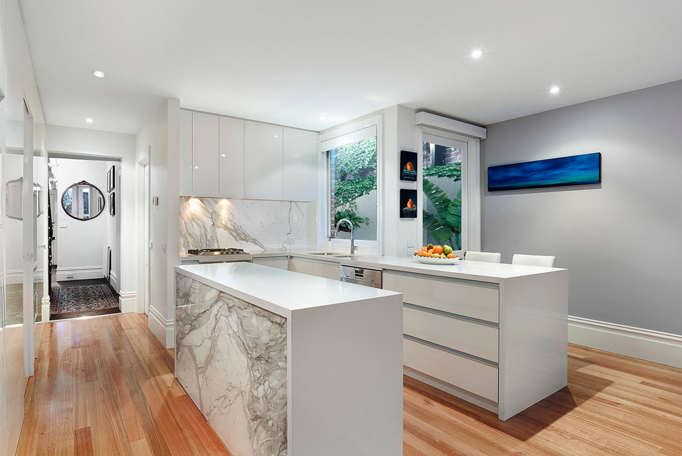 Inspiration for a mid-sized contemporary l-shaped open plan kitchen in Melbourne with an undermount sink, flat-panel cabinets, white cabinets, marble benchtops, grey splashback, stone slab splashback, stainless steel appliances, light hardwood floors and multiple islands.