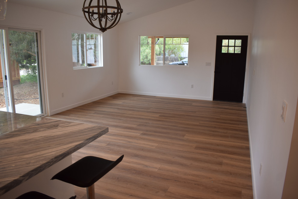 Example of a large cottage open concept laminate floor, brown floor and vaulted ceiling living room design in Santa Barbara with white walls, no fireplace and a wall-mounted tv