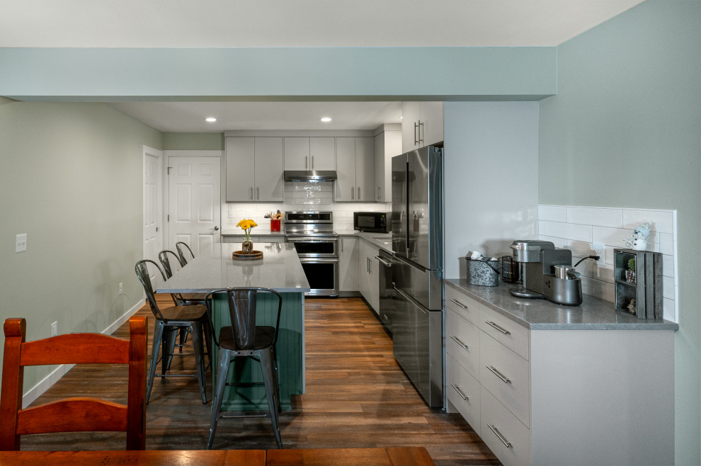 Design ideas for a mid-sized contemporary l-shaped eat-in kitchen in Seattle with an undermount sink, flat-panel cabinets, grey cabinets, quartz benchtops, white splashback, ceramic splashback, stainless steel appliances, vinyl floors, with island, brown floor and grey benchtop.