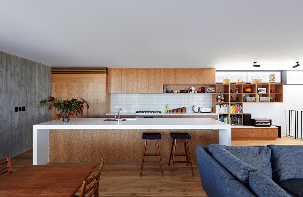 This is an example of a midcentury galley open plan kitchen in Los Angeles with a double-bowl sink, flat-panel cabinets, medium wood cabinets, white splashback, mosaic tile splashback, panelled appliances, medium hardwood floors, with island, brown floor and white benchtop.