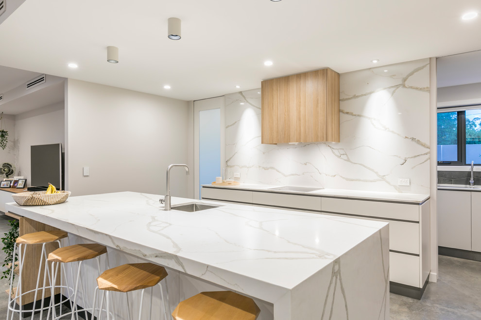Design ideas for a large modern galley kitchen pantry in Canberra - Queanbeyan with an undermount sink, flat-panel cabinets, white cabinets, quartz benchtops, white splashback, stone slab splashback, black appliances, concrete floors, with island, grey floor and white benchtop.