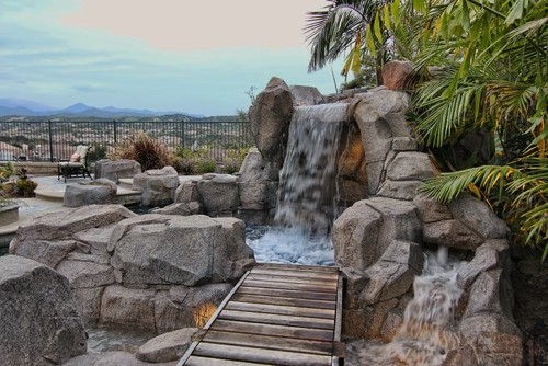 Photo of a mid-sized tropical backyard lap pool in Orange County with a hot tub and natural stone pavers.