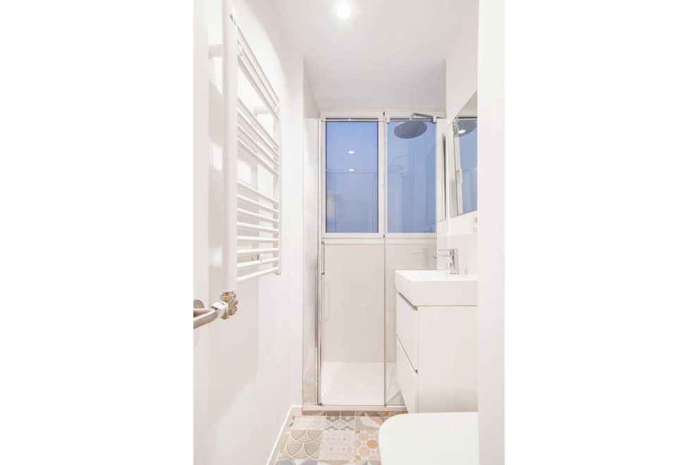 На фото: маленькая, узкая и длинная ванная комната в скандинавском стиле с фасадами с утопленной филенкой, белыми фасадами, душем без бортиков, инсталляцией, белой плиткой, керамической плиткой, белыми стенами, полом из керамической плитки, душевой кабиной, монолитной раковиной, столешницей из искусственного камня, разноцветным полом, душем с распашными дверями, белой столешницей, тумбой под одну раковину и подвесной тумбой для на участке и в саду с
