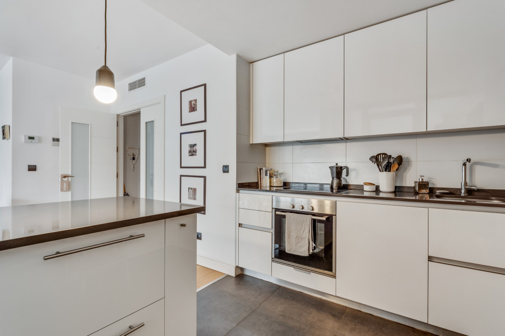 Design ideas for a mid-sized scandinavian galley eat-in kitchen in Madrid with a single-bowl sink, flat-panel cabinets, white cabinets, granite benchtops, grey splashback, metal splashback, stainless steel appliances, porcelain floors, with island, grey floor and grey benchtop.