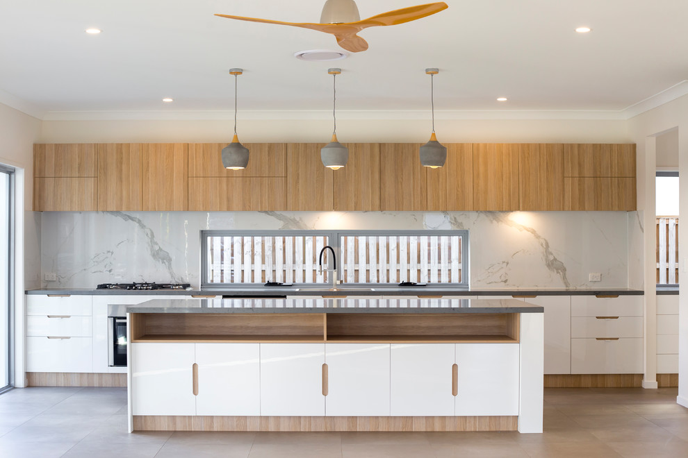 This is an example of a contemporary galley kitchen in Brisbane with flat-panel cabinets, white cabinets, stone slab splashback, stainless steel appliances, with island, beige floor and grey benchtop.