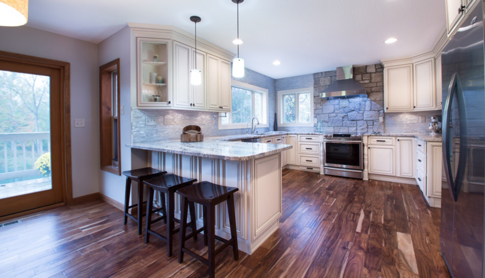 Open concept kitchen - mid-sized transitional u-shaped dark wood floor and brown floor open concept kitchen idea in Orlando with an undermount sink, recessed-panel cabinets, white cabinets, granite countertops, gray backsplash, stone tile backsplash, stainless steel appliances, an island and gray countertops