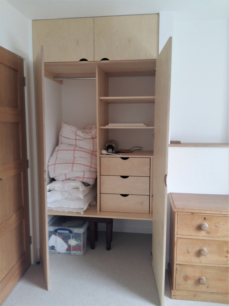 Photo of an expansive scandinavian storage and wardrobe in Cornwall with flat-panel cabinets, light wood cabinets, carpet and grey floor.