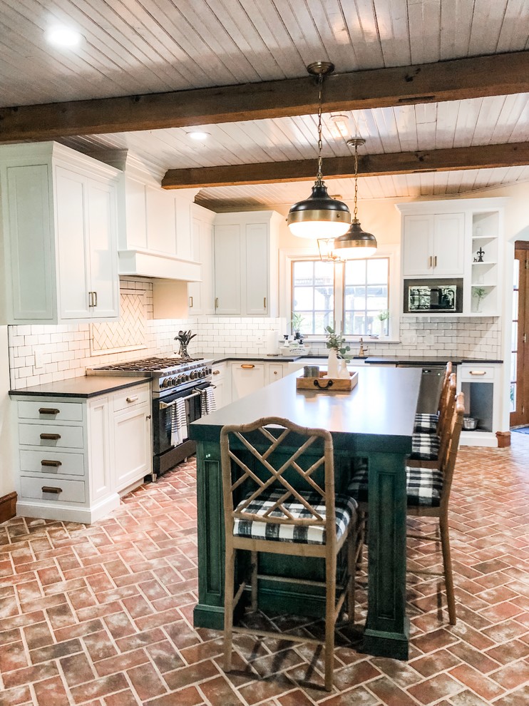 Inspiration for a mid-sized country u-shaped eat-in kitchen in Philadelphia with a farmhouse sink, recessed-panel cabinets, white cabinets, soapstone benchtops, white splashback, subway tile splashback, stainless steel appliances, brick floors, with island, red floor and black benchtop.