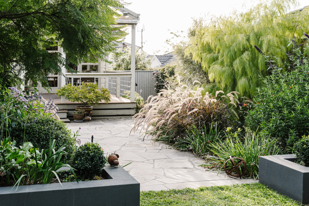 На фото: солнечный, летний засухоустойчивый сад среднего размера на заднем дворе в современном стиле с клумбами, хорошей освещенностью, покрытием из каменной брусчатки и с деревянным забором