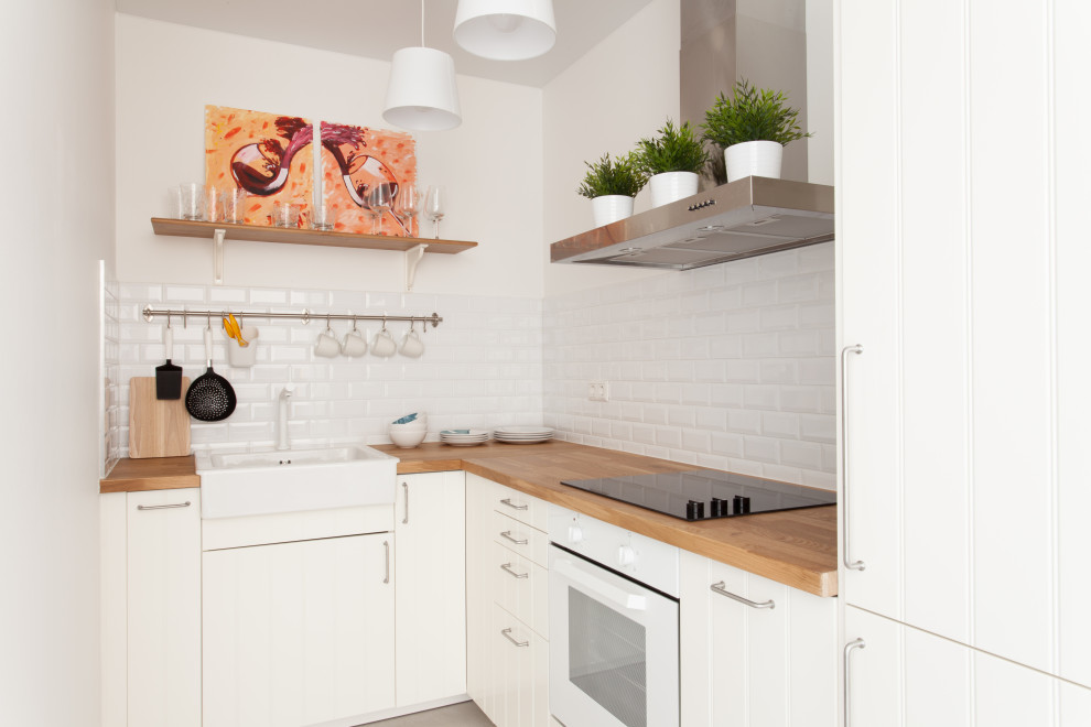 Scandinavian l-shaped kitchen in Saint Petersburg with a farmhouse sink, flat-panel cabinets, white cabinets, wood benchtops, white splashback, subway tile splashback, no island, grey floor and brown benchtop.