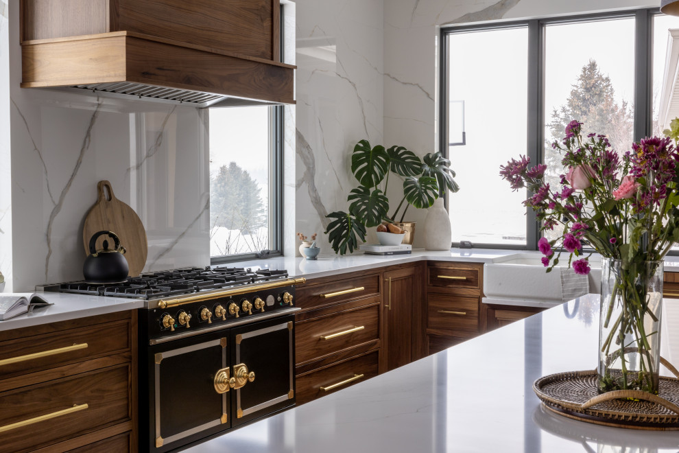 Example of a mid-sized transitional l-shaped light wood floor and brown floor eat-in kitchen design with a farmhouse sink, shaker cabinets, blue cabinets, quartz countertops, white backsplash, quartz backsplash, black appliances, an island and white countertops