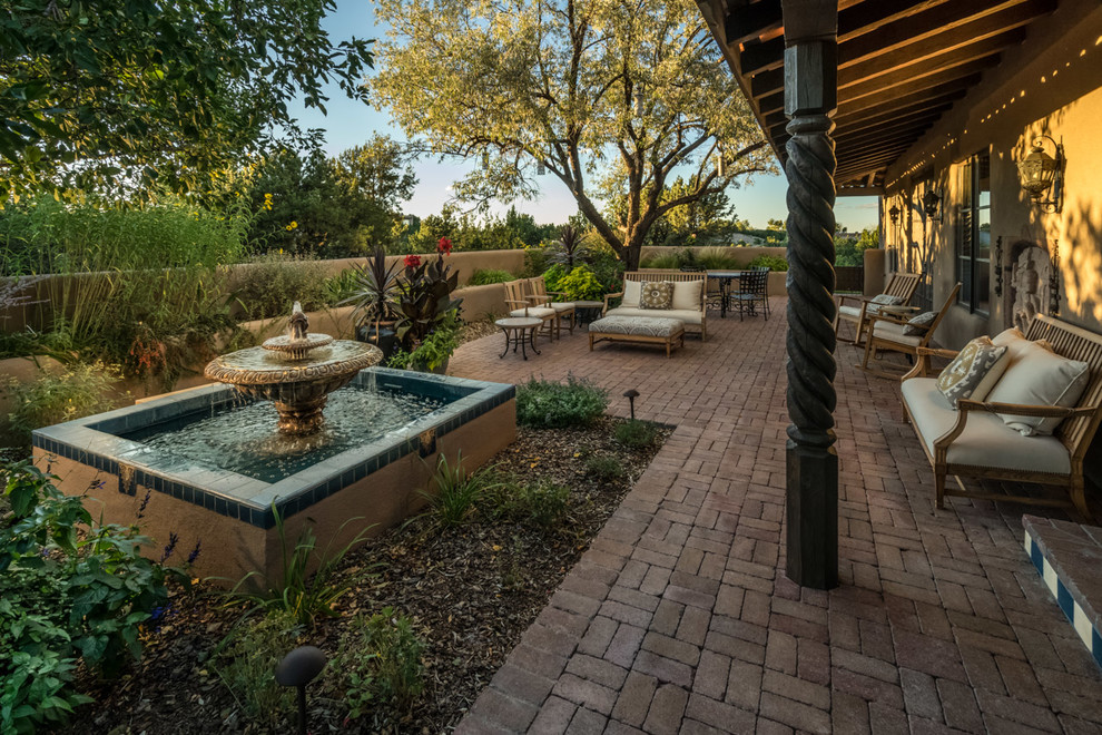 Mid-sized mediterranean courtyard patio in Albuquerque with brick pavers, a roof extension and a water feature.