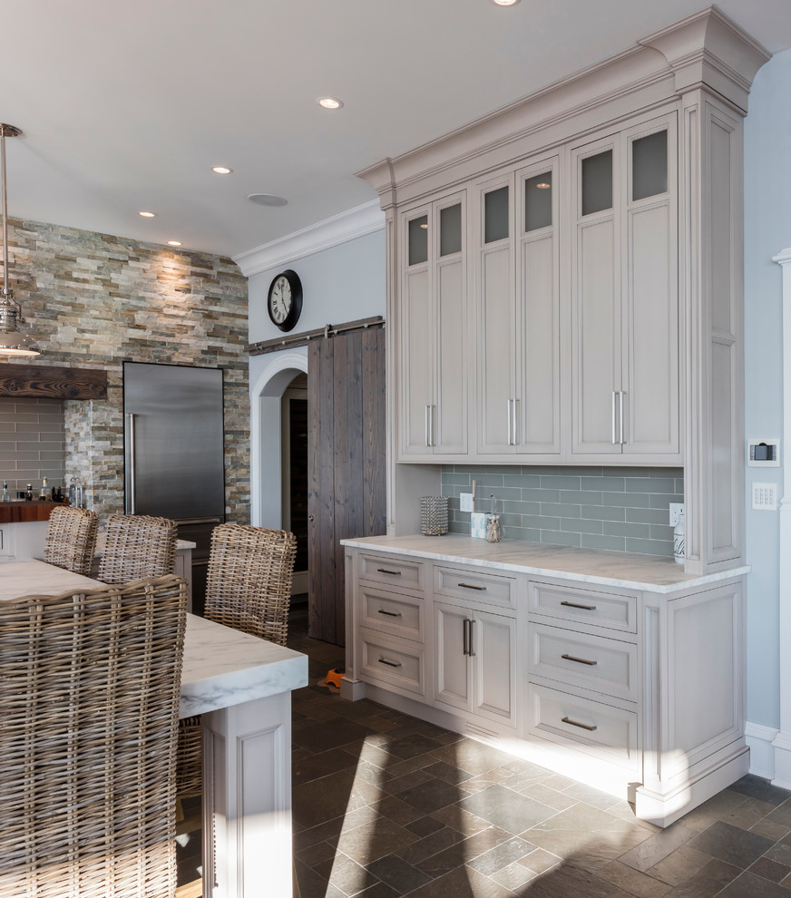 Large beach style single-wall eat-in kitchen in Philadelphia with a farmhouse sink, recessed-panel cabinets, grey cabinets, marble benchtops, grey splashback, glass tile splashback, stainless steel appliances, slate floors and with island.