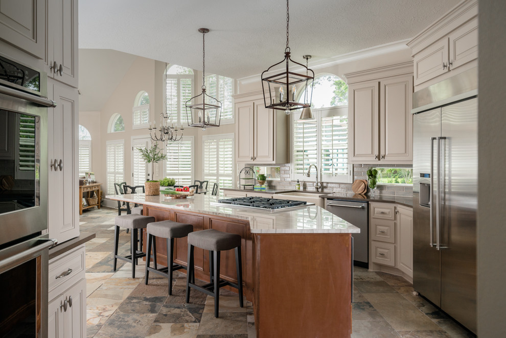 Inspiration for a mid-sized transitional l-shaped kitchen in Houston with a farmhouse sink, raised-panel cabinets, beige cabinets, grey splashback, stainless steel appliances, with island, slate floors, multi-coloured floor, quartzite benchtops, subway tile splashback and brown benchtop.